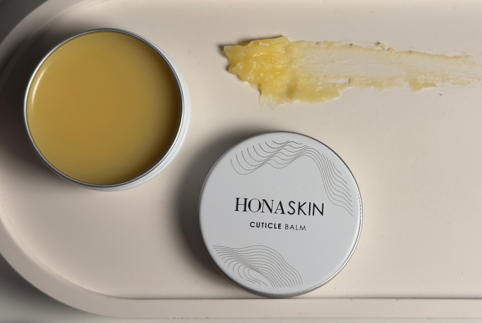 Honaskin cuticle balm with a lid on a beige surface
